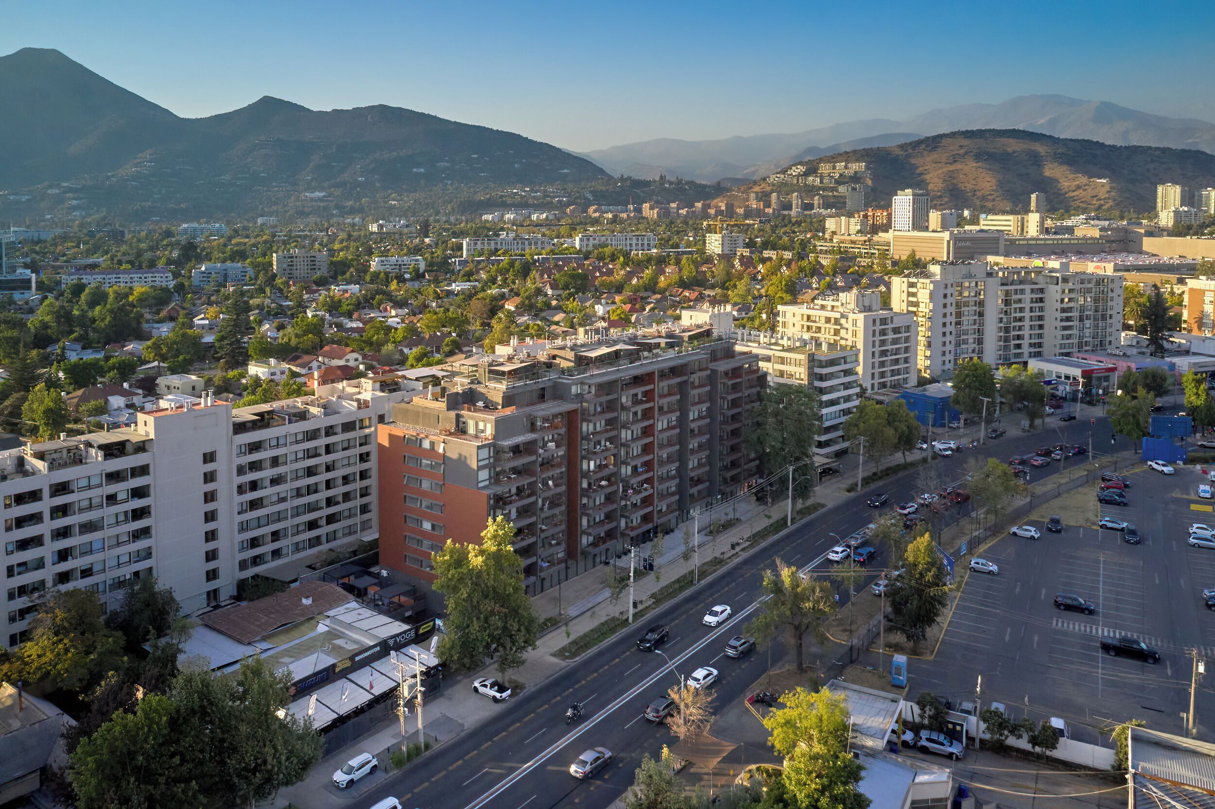 Un paisaje urbano con edificios de varios pisos, una avenida amplia y montañas a lo lejos.