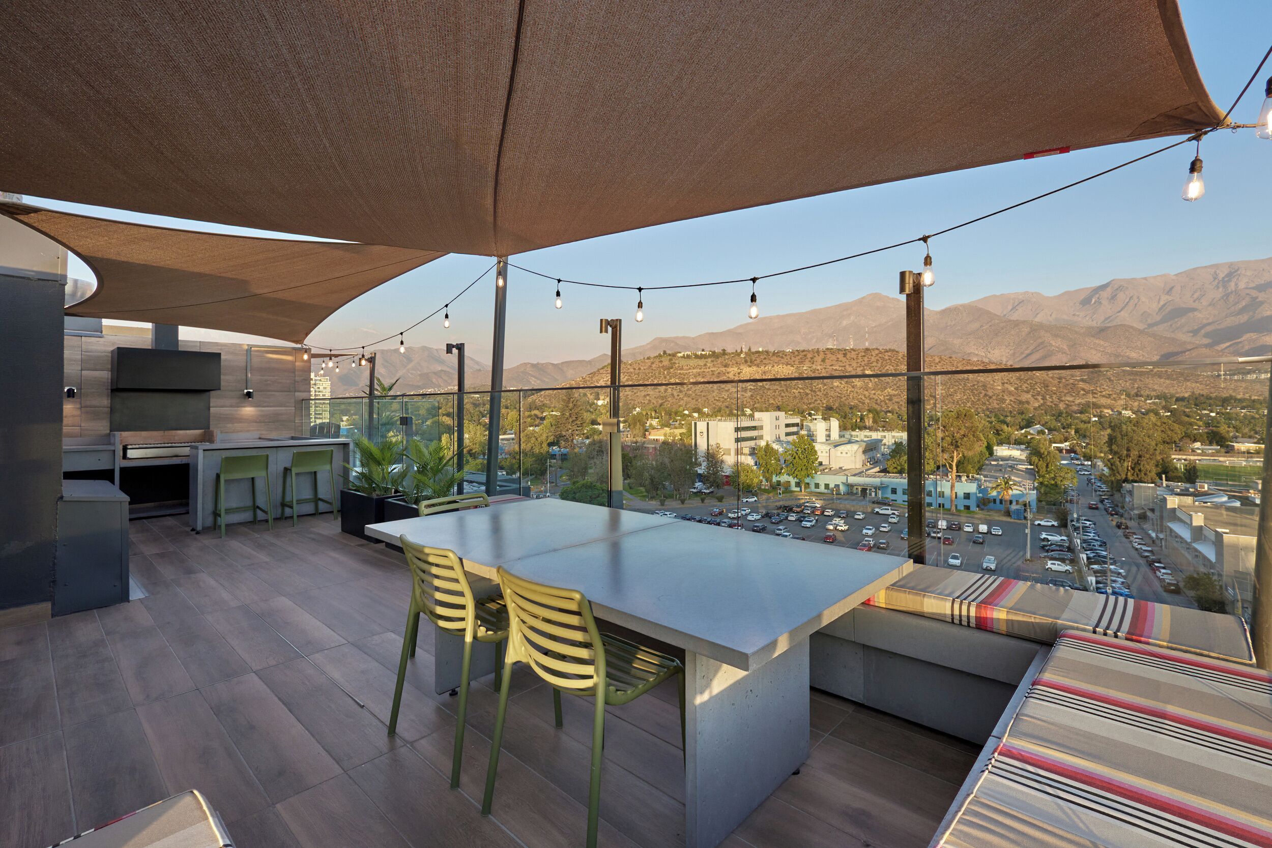 A modern outdoor dining area with a large table and chairs, a barbecue grill, and a view of the city and mountains.