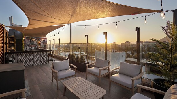 Een terras op het dak met een bar, zitplaatsen en uitzicht op de skyline bij zonsondergang.