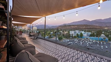 Una terraza con mobiliario, vistas a montañas y un estacionamiento.