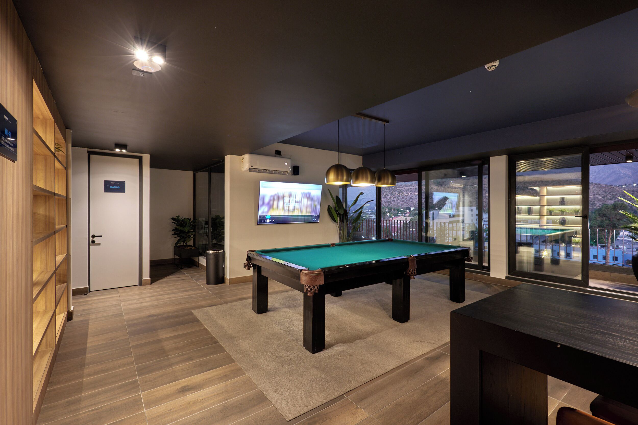 Een pooltafel in een moderne kamer met een televisie, een deur en een uitzicht door grote ramen.