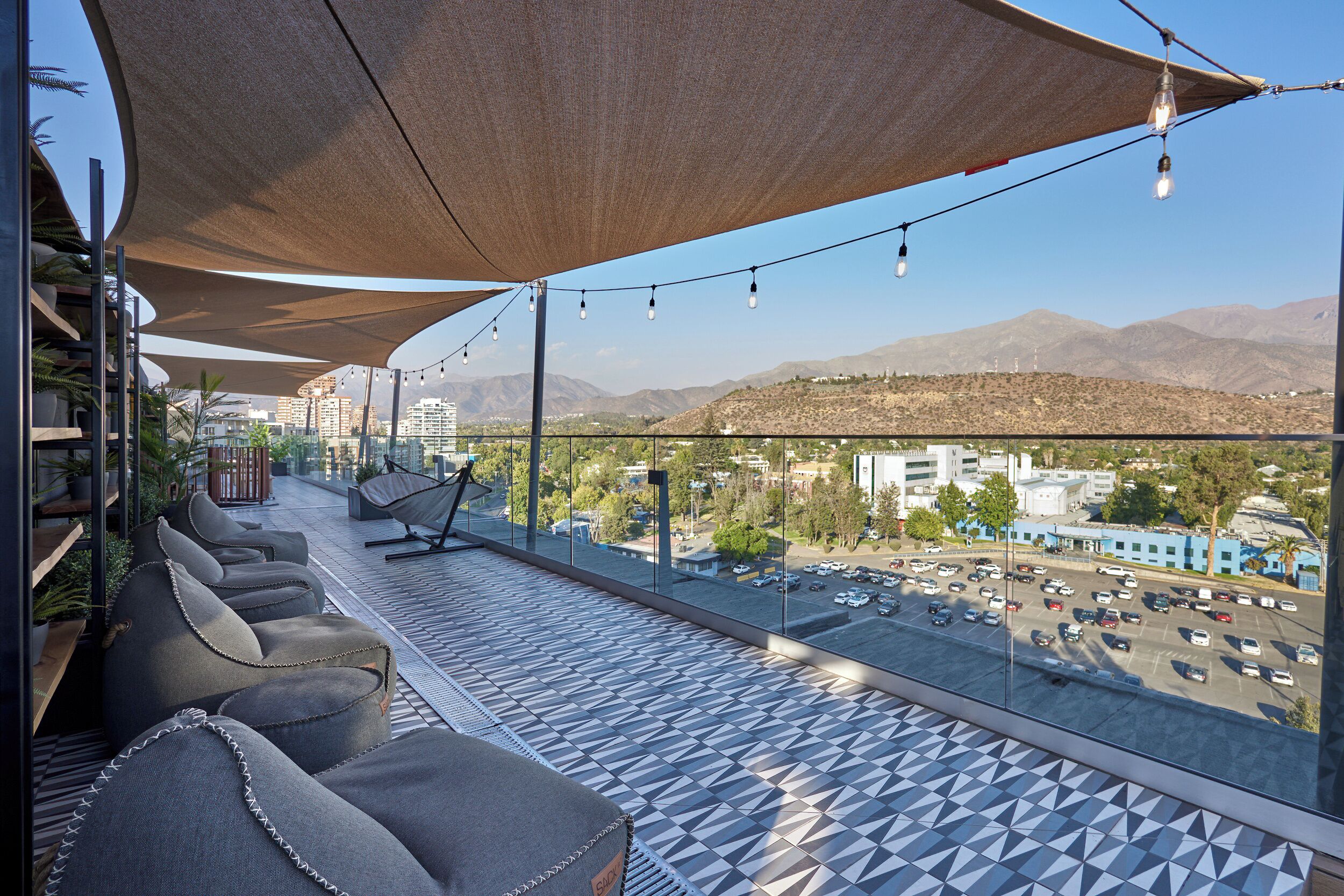 A balcony with seating, a view of a parking lot, and distant mountains.