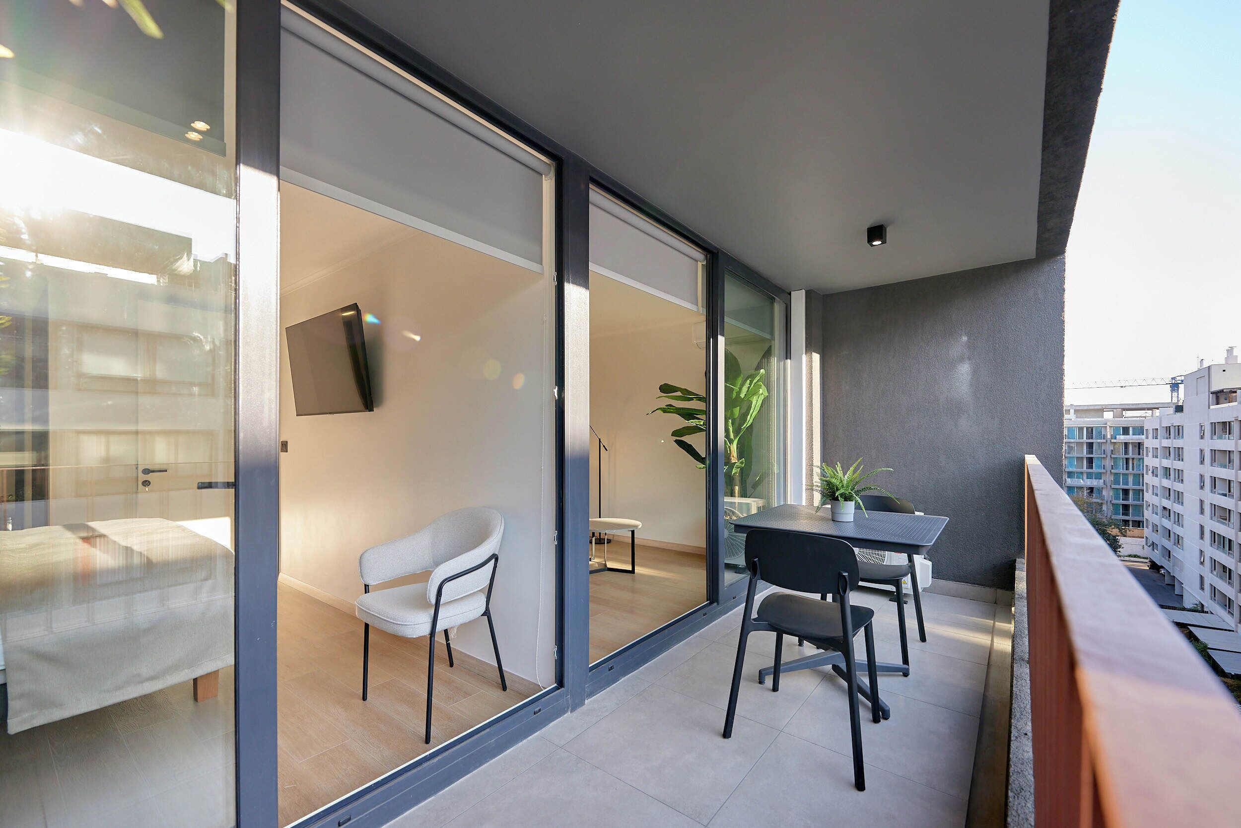 A modern balcony with a dining table, chairs, a TV, and a potted plant.