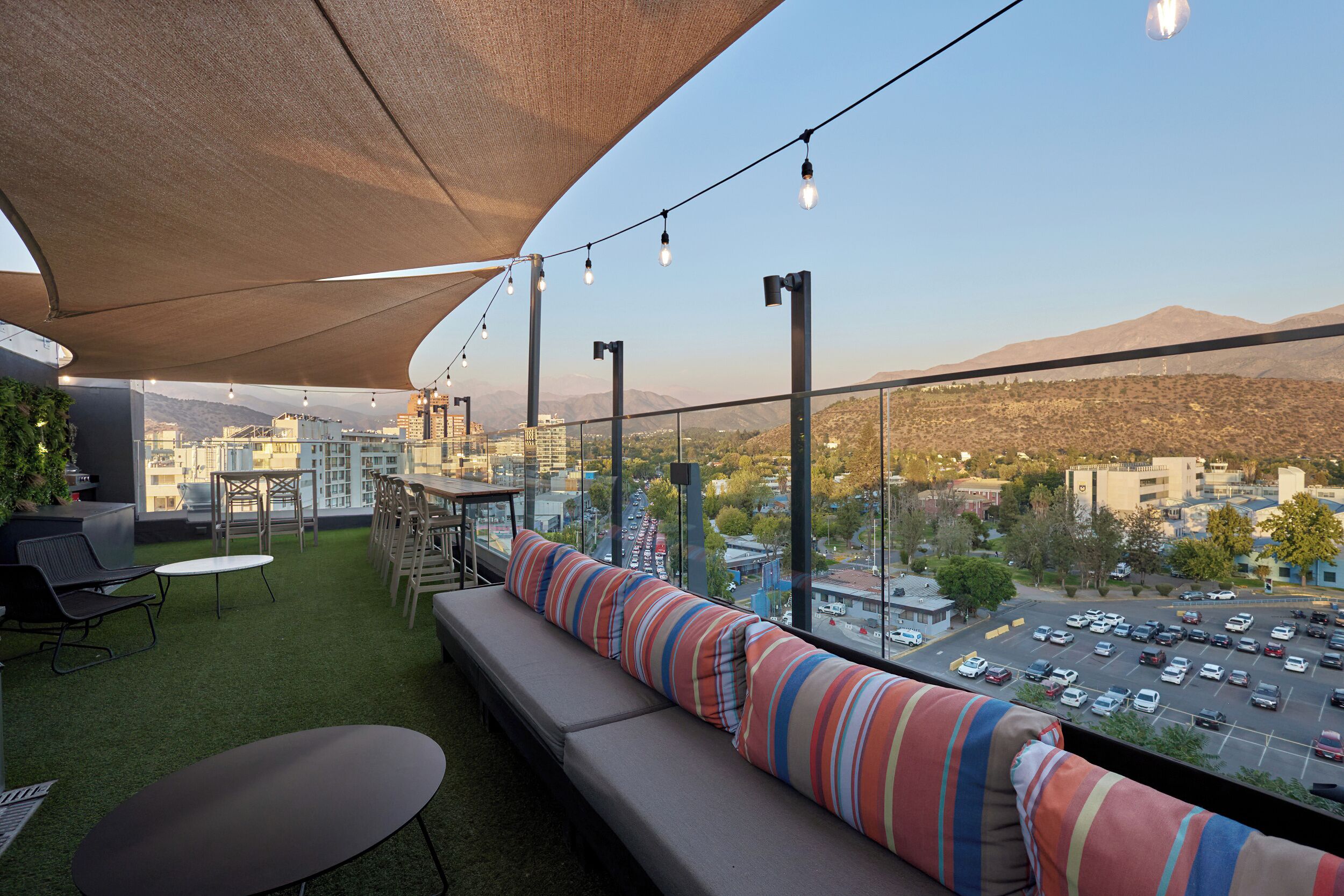 Une terrasse sur le toit, aménagée avec un canapé, des chaises, une table et offrant une vue sur un parking et le paysage urbain.
