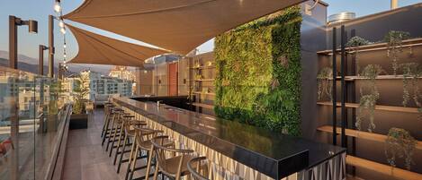 A rooftop bar with a green wall, bar stools, and a view of the cityscape.