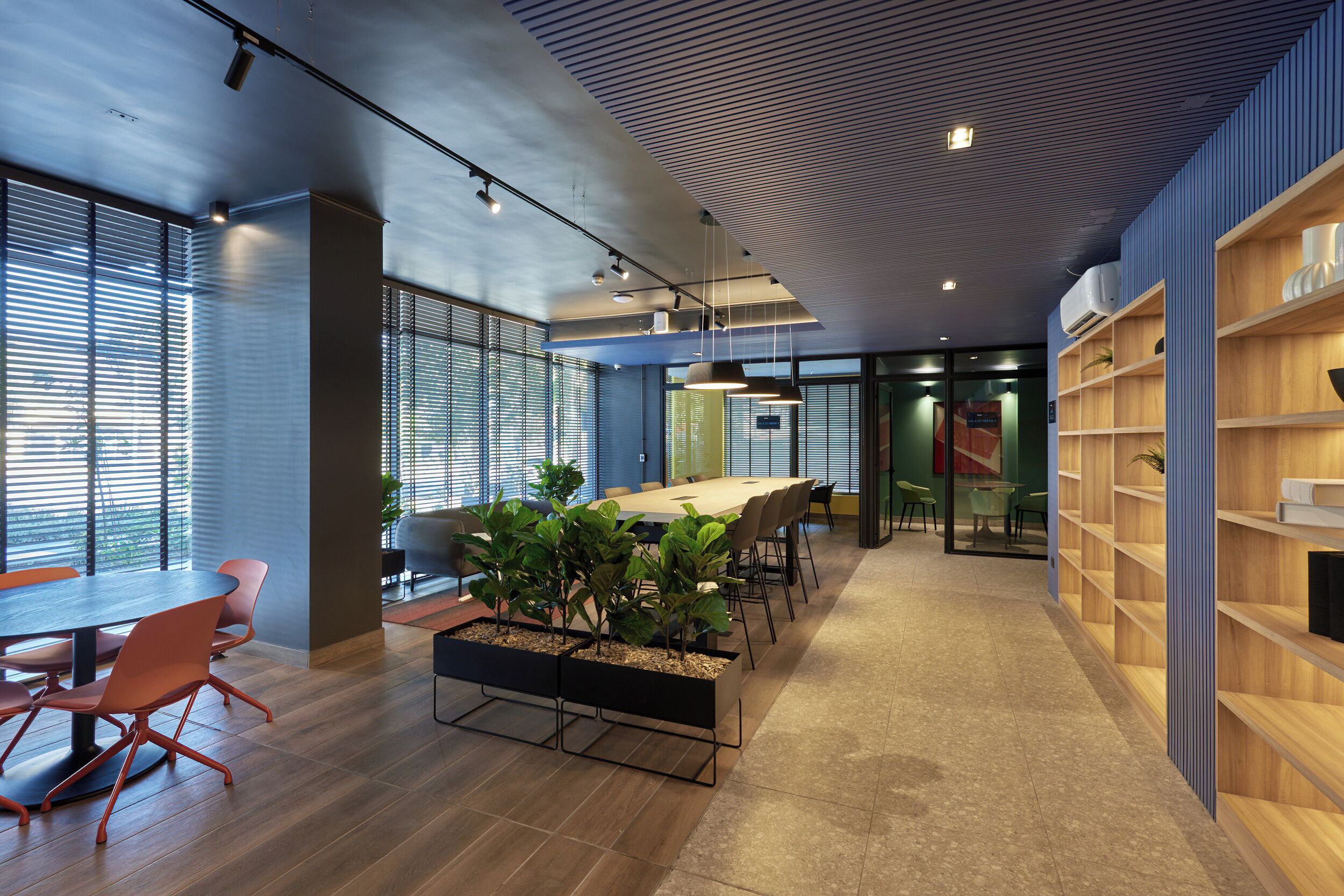 A modern office space with a long table, chairs, potted plants, and shelves.