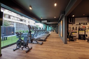 Ein Fitnessstudio mit Laufbändern, Ergometer und Krafttrainingsgeräten, großen Fenstern und Blick auf ein Gebäude.