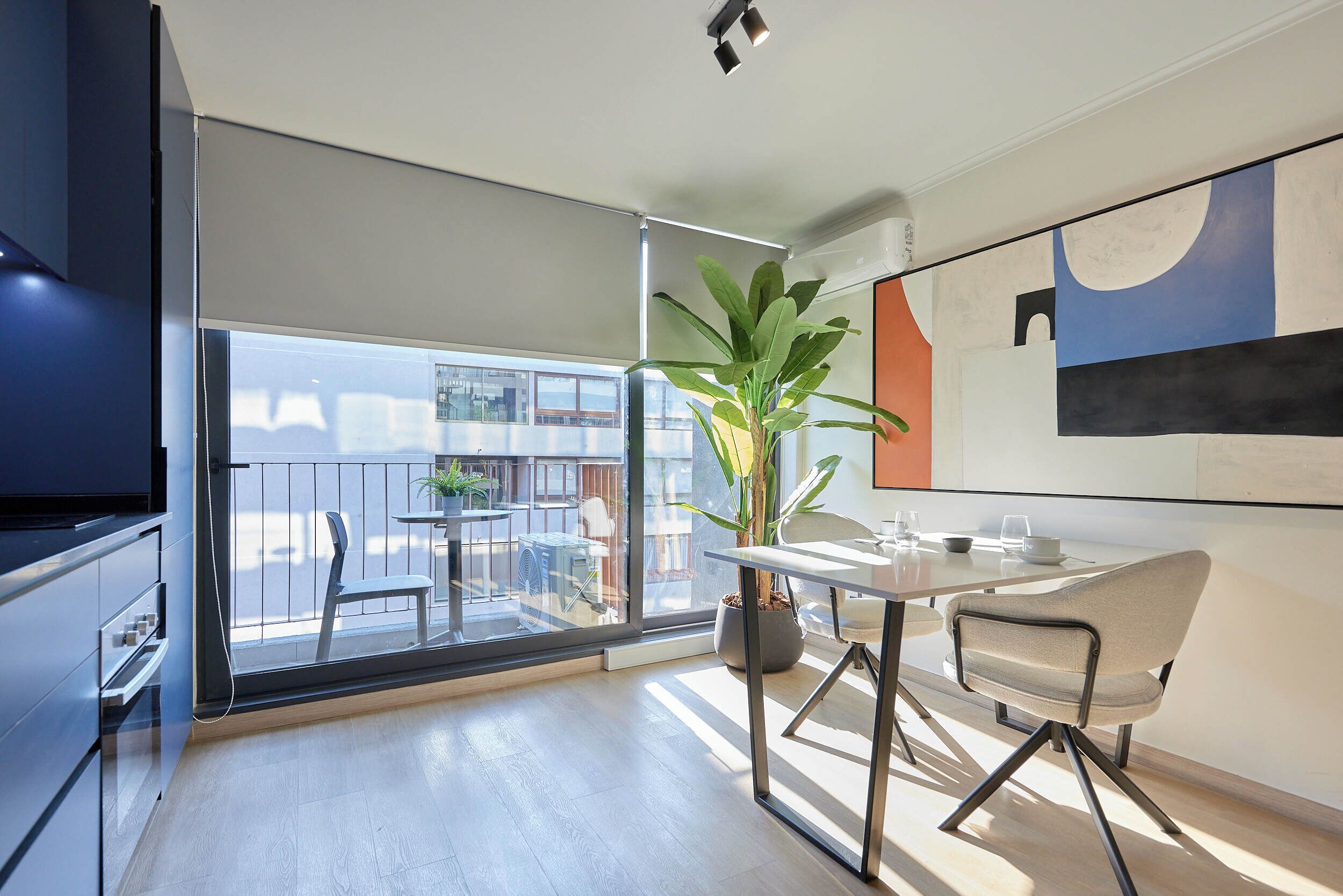 Una cocina moderna con un ventanal grande, una zona de comedor con mesa y sillas, y una planta en maceta.