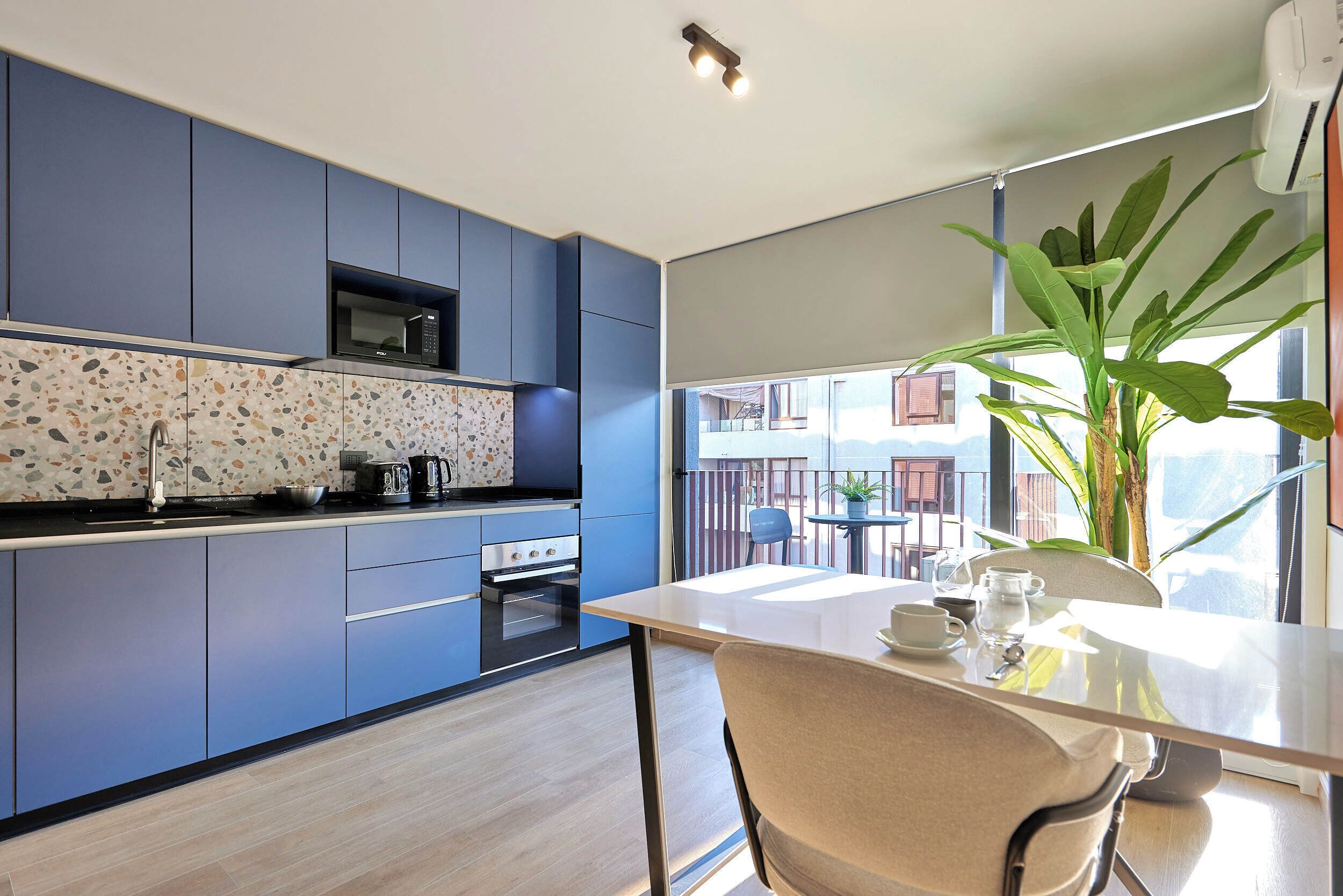 Una cocina moderna con armarios azules, un microondas y una estufa. Hay una mesa de comedor con sillas y una planta grande en maceta.