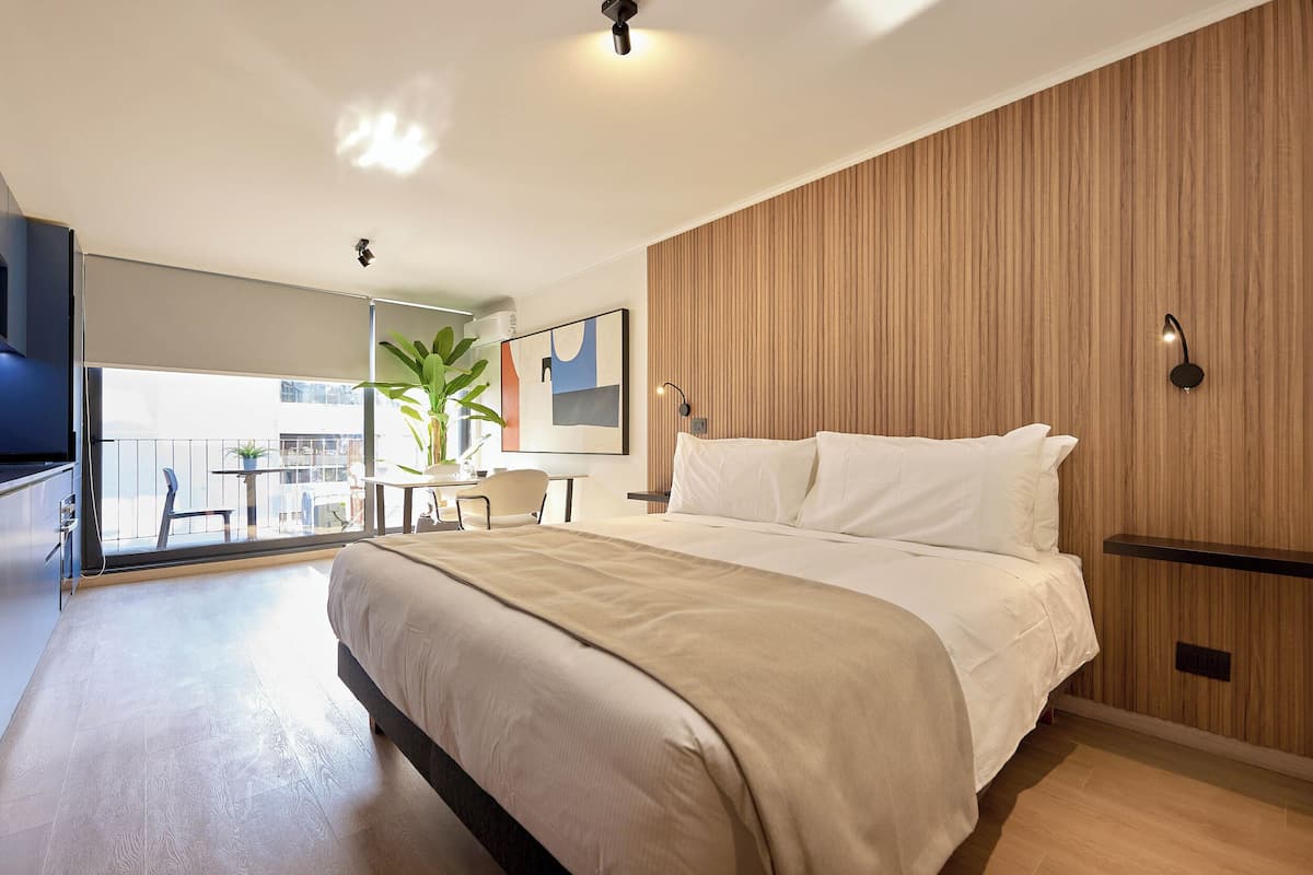 Ein modernes Hotelzimmer mit einem großen Bett, einem Schreibtisch, einem Sessel, einer Zimmerpflanze und Blick auf die Stadt.