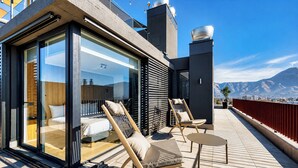 Een moderne hotelkamer met een glazen schuifpui, een bed en een balkon met zitplaatsen.