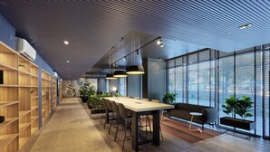 Een moderne vergaderruimte met een lange tafel, stoelen en een bank. Er staan plantenbakken en een groot raam met zonwering.