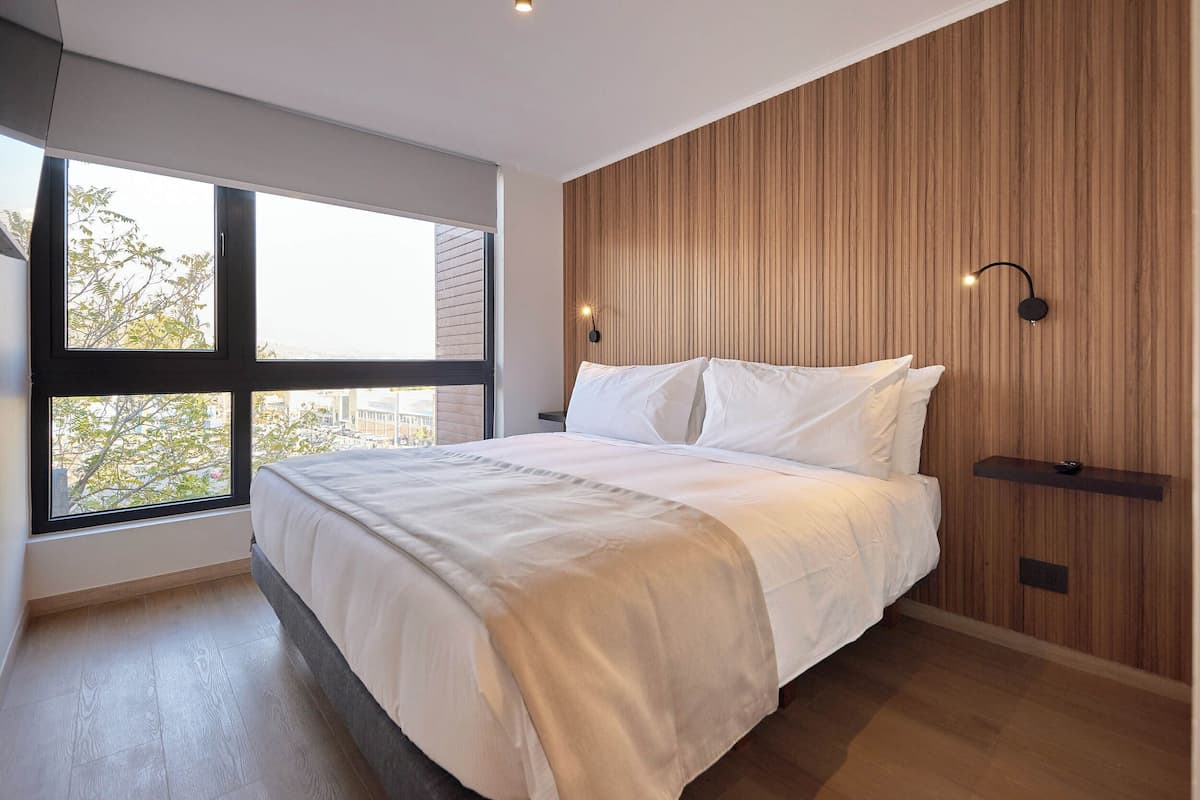 Ein Schlafzimmer mit großem Fenster, einem Bett mit weißer Bettwäsche, einer Holzvertäfelung und einer Wandleuchte.