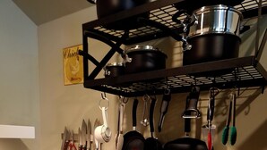 Cocina con encimera de granito, tostadora, cafetera, ollas y sartenes colgantes y un estante de pared.