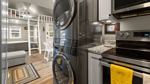 Cocina compacta con lavadora y secadora apiladas, microondas, horno y una pequeña encimera.