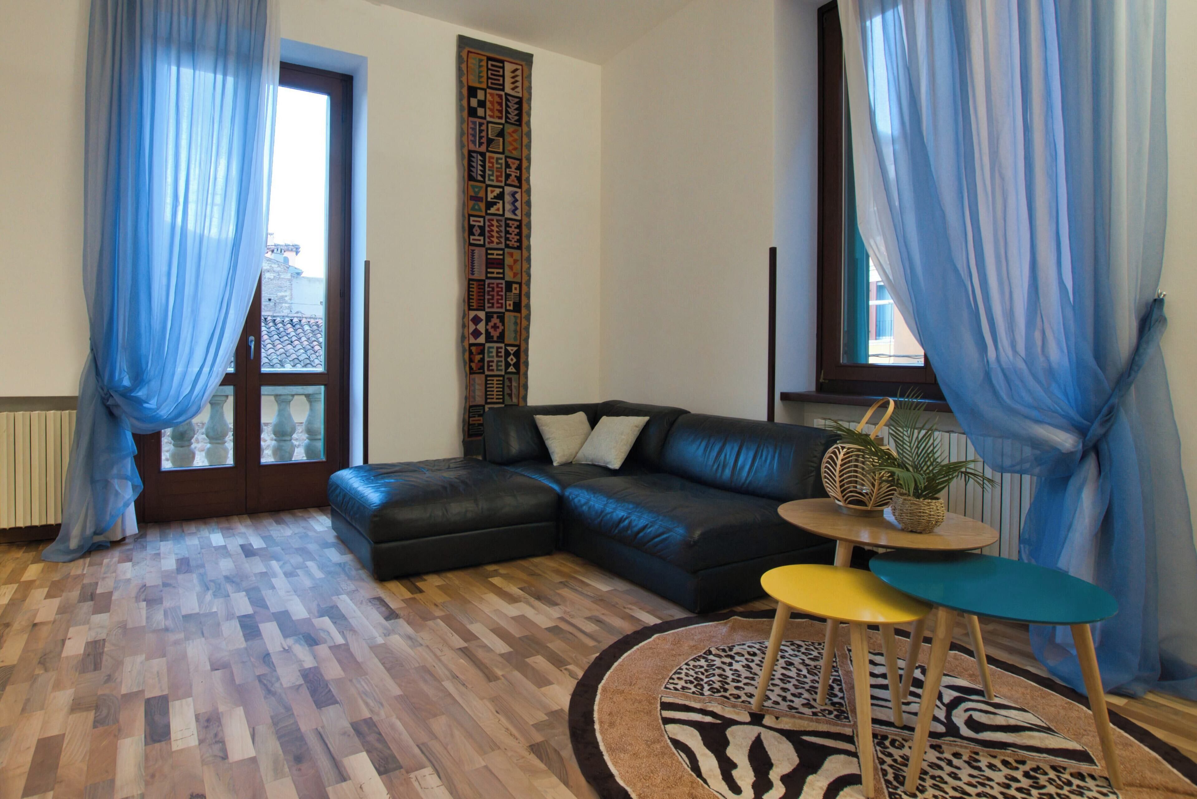 Un soggiorno moderno con un divano componibile, un tavolino rotondo con sedie, un tappeto decorato e tende blu.