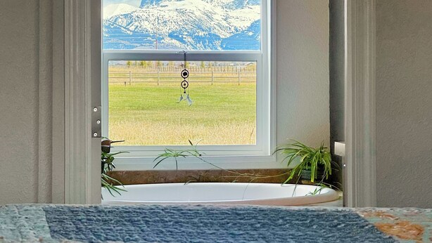 Een deuropening die leidt naar een kamer met een groot raam met uitzicht op besneeuwde bergen en een grasveld.