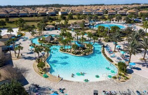 En stor swimmingpool omgivet af palmer og liggestole, med udsigt til boligbygninger i baggrunden.