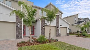 A modern residential building with a garage, a red door, and a well-maintained lawn with palm trees. - Stylish 3BR Condo Championsgate w Water Park (Davenport)