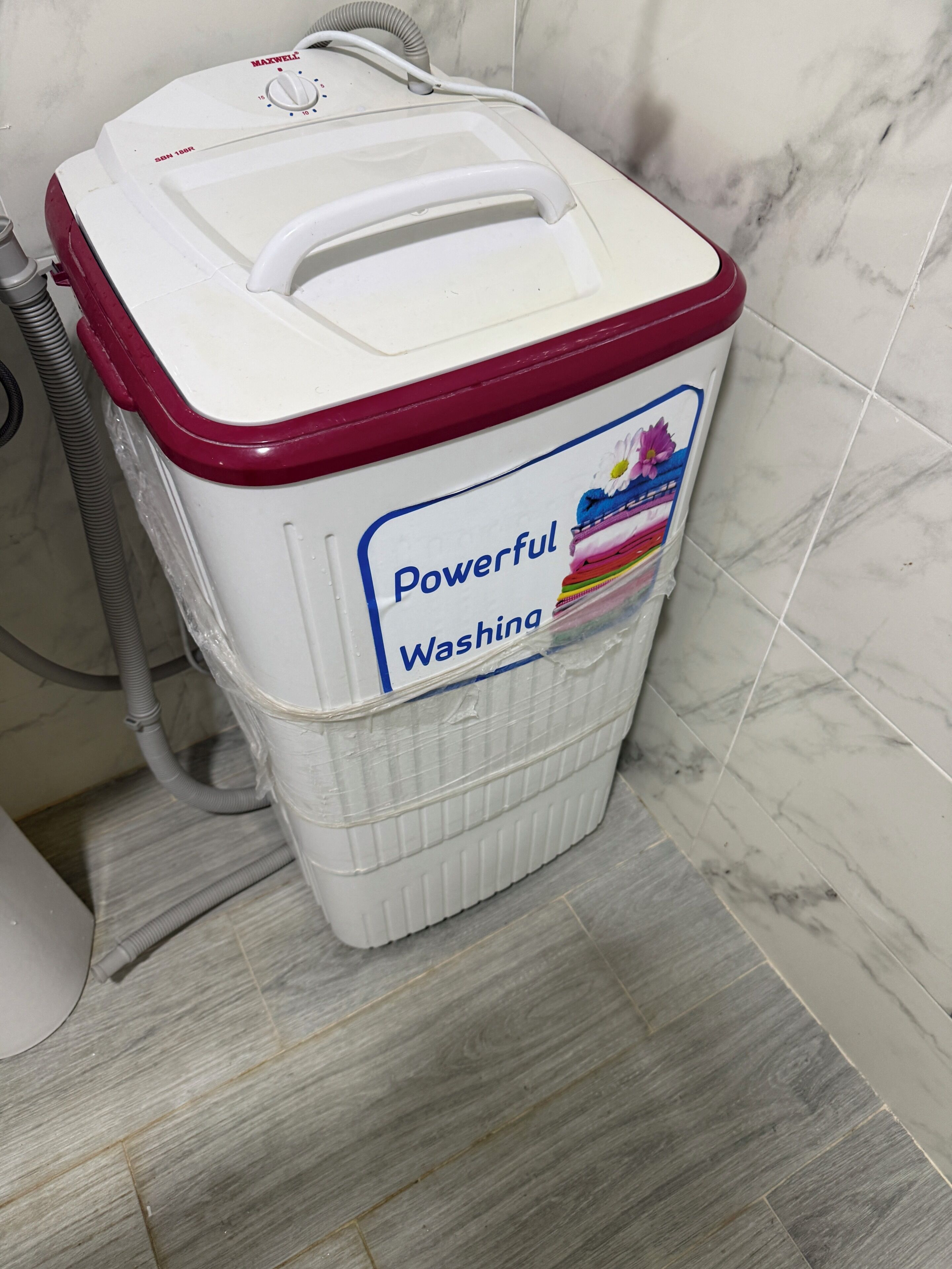 A white and red laundry basket labeled 'Powerful Washing' in a bathroom with marble tiles.