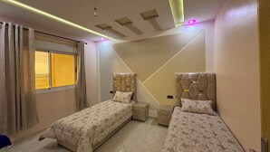 Une chambre avec deux lits, une fenêtre avec des rideaux, un plafond doté d’un éclairage encastré et un téléviseur fixé au mur.
