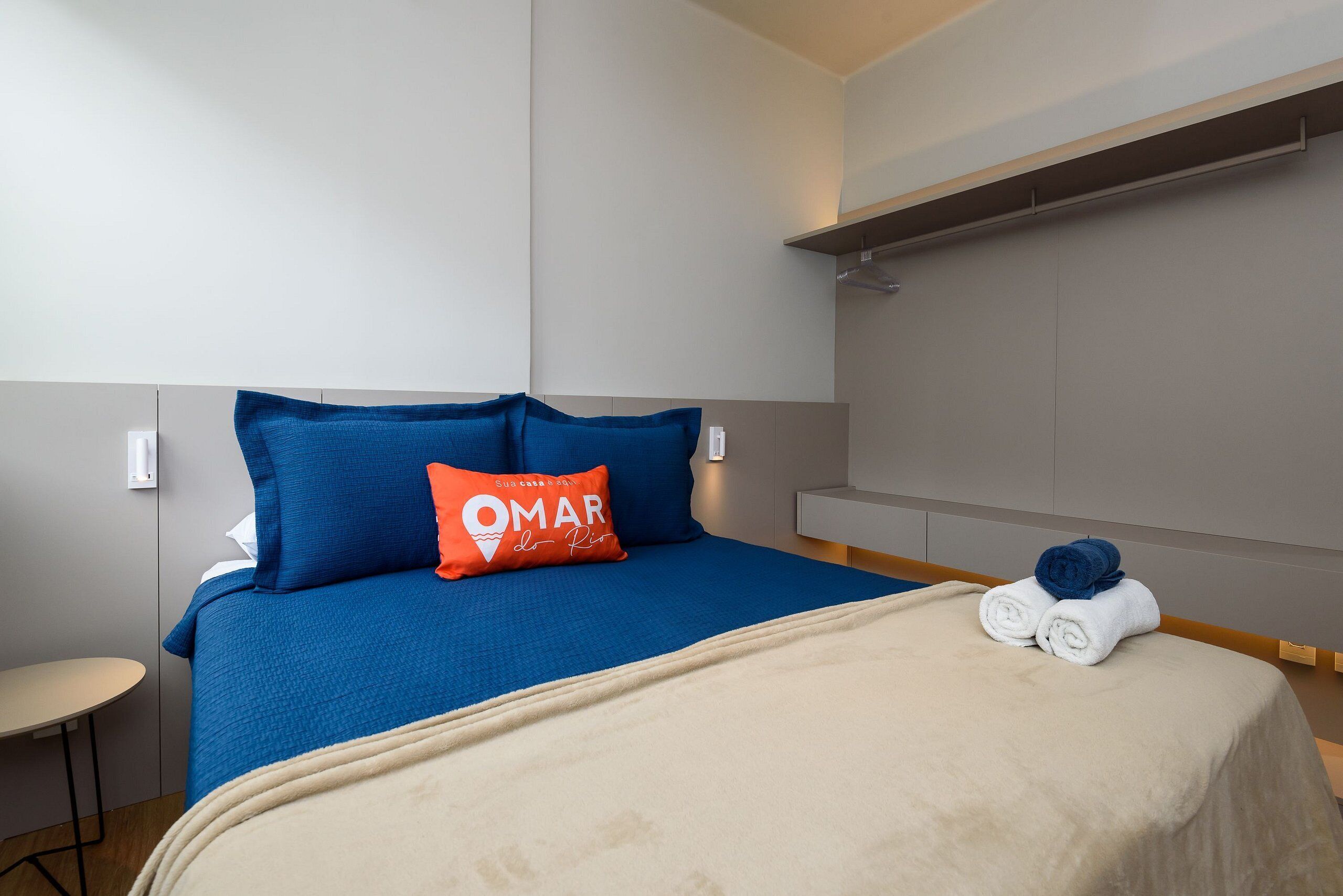 Ett hotellrum med en säng, ett litet bord och en handduksställning.