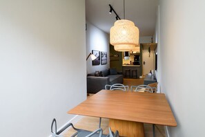 Ett modernt matområde med ett träbord och stolar, en hängande lampa av rotting och ett kök i bakgrunden.