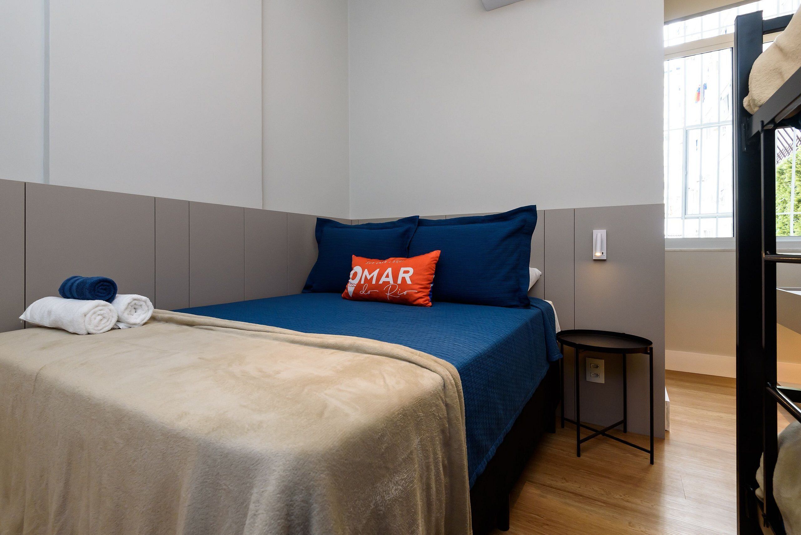 Una cama bien hecha con una colcha azul y beige, dos almohadas y toallas enrolladas a un lado.