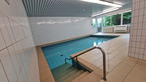 Une piscine dont les parois sont recouvertes de carreaux et qui est équipée d’une rampe métallique.