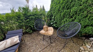 Une terrasse de jardin avec deux chaises en fil de fer noir, une table en bois et une petite plante en pot.