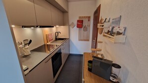 Une cuisine compacte équipée d’une cuisinière, d’un évier et de placards. On y trouve également un petit coin repas avec une table et des chaises.