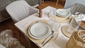 Une table à manger dressée avec des assiettes, des verres et des couverts, entourée de sets de table en fibres tressées et d’une chaise en bois.