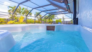 Ein Whirlpool mit Glasverkleidung, umgeben von üppigem Grün und blauem Himmel.