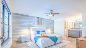 Ein modernes Schlafzimmer mit einem großen Bett, einem Deckenventilator und Blick in das angrenzende Badezimmer.