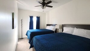 Habitación de hotel con dos camas, ventilador de techo, perchero y ventana con cortinas.