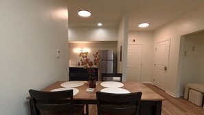 Un comedor con una mesa de madera y cuatro sillas, un florero con flores, y una cocina al fondo.