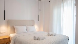 Ein ordentlich bezogenes Bett mit zwei zusammengerollten Handtüchern, einem Nachttisch und einer Deckenleuchte.