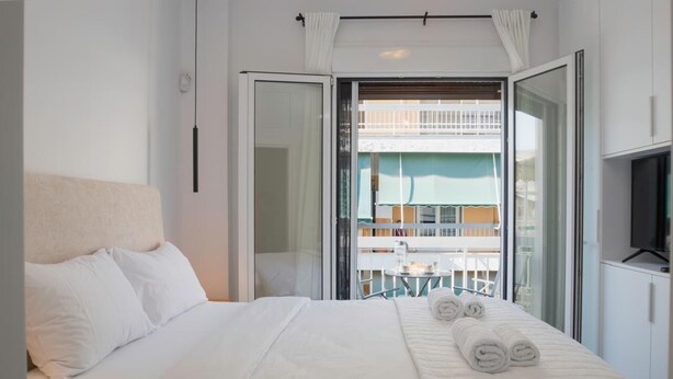Ein Hotelzimmer mit Bett, Fernseher und einem Balkon mit Blick auf ein Gebäude.
