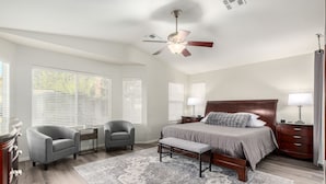 A bedroom with a large bed, two bedside tables, a nightstand, a chair, a bench, a ceiling fan, and a patterned rug. - Private Pool & Patio: Home in Surprise! (Surprise)