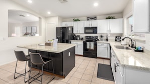 A modern kitchen with white cabinets, a black refrigerator, a microwave, and a coffee maker. There are two bar stools and a small island with a countertop. - Private Pool & Patio: Home in Surprise! (Surprise)
