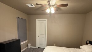 A bedroom with a bed, a dresser, a ceiling fan, a door, and a window with blinds.