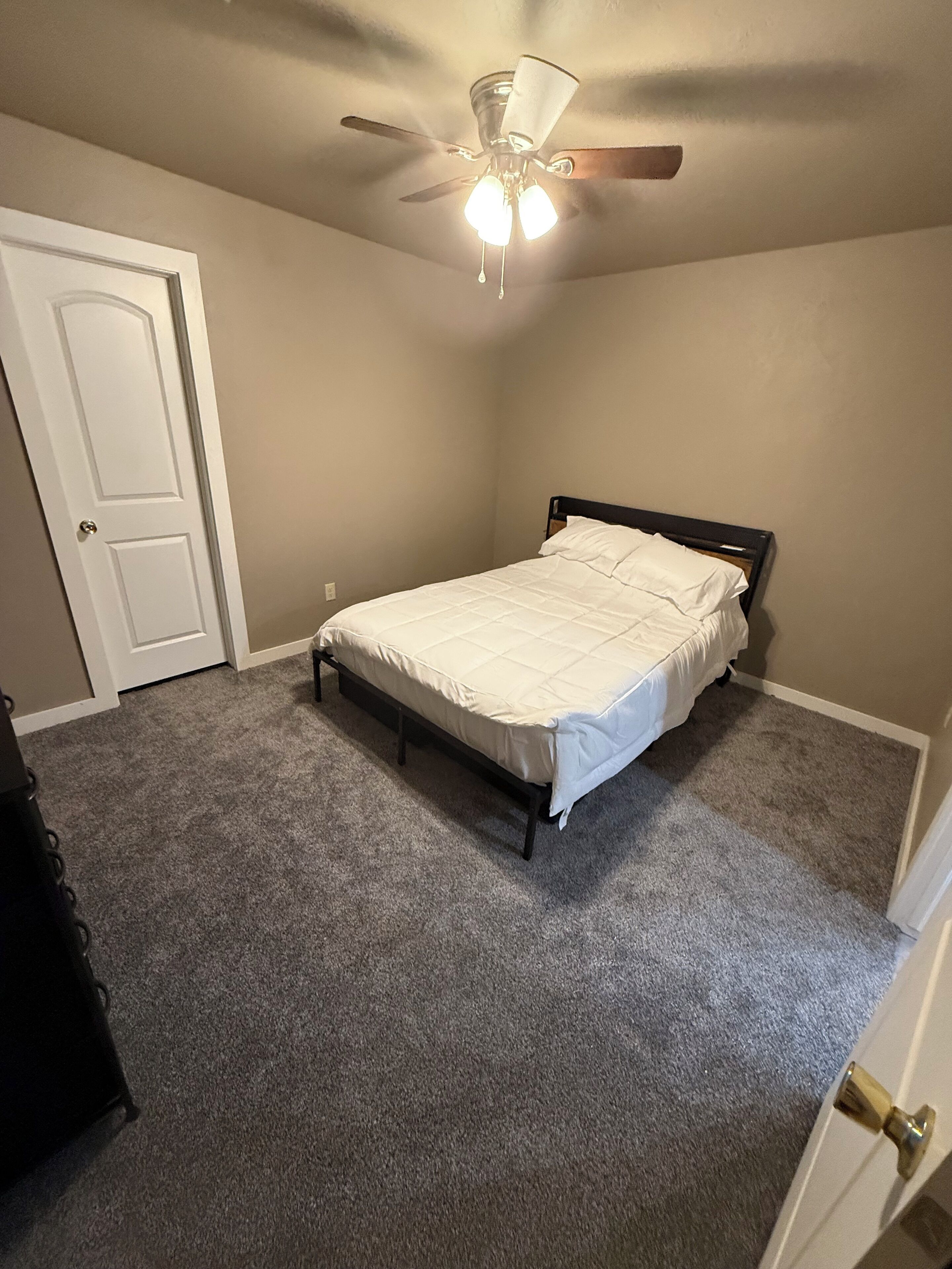 Een slaapkamer met een bed, een plafondventilator en vloerbedekking.