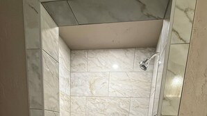 A shower with marble tiles and a pebble-patterned floor.