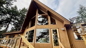 A modern wooden cabin with a steeply pitched roof, large windows, and a deck with a wooden railing. - Peaceful Forest Retreat w/ Water Views & Stove (San Juan County)