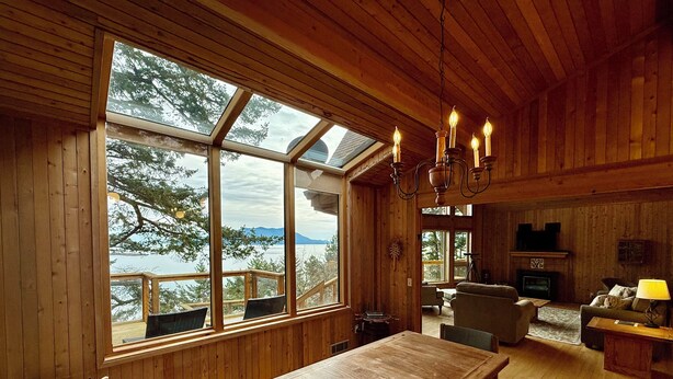 A wooden cabin interior with a dining area, seating, and a fireplace. - Peaceful Forest Retreat w/ Water Views & Stove (San Juan County)