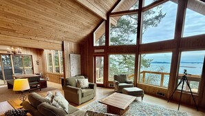 A spacious living room with a large sofa, armchairs, and a coffee table. There are large windows offering a view of the outdoors. - Peaceful Forest Retreat w/ Water Views & Stove (San Juan County)