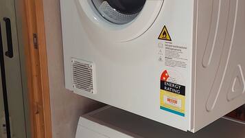 Two stacked front-loading washing machines, one on top of the other, in a room with wooden flooring and a door visible in the background.