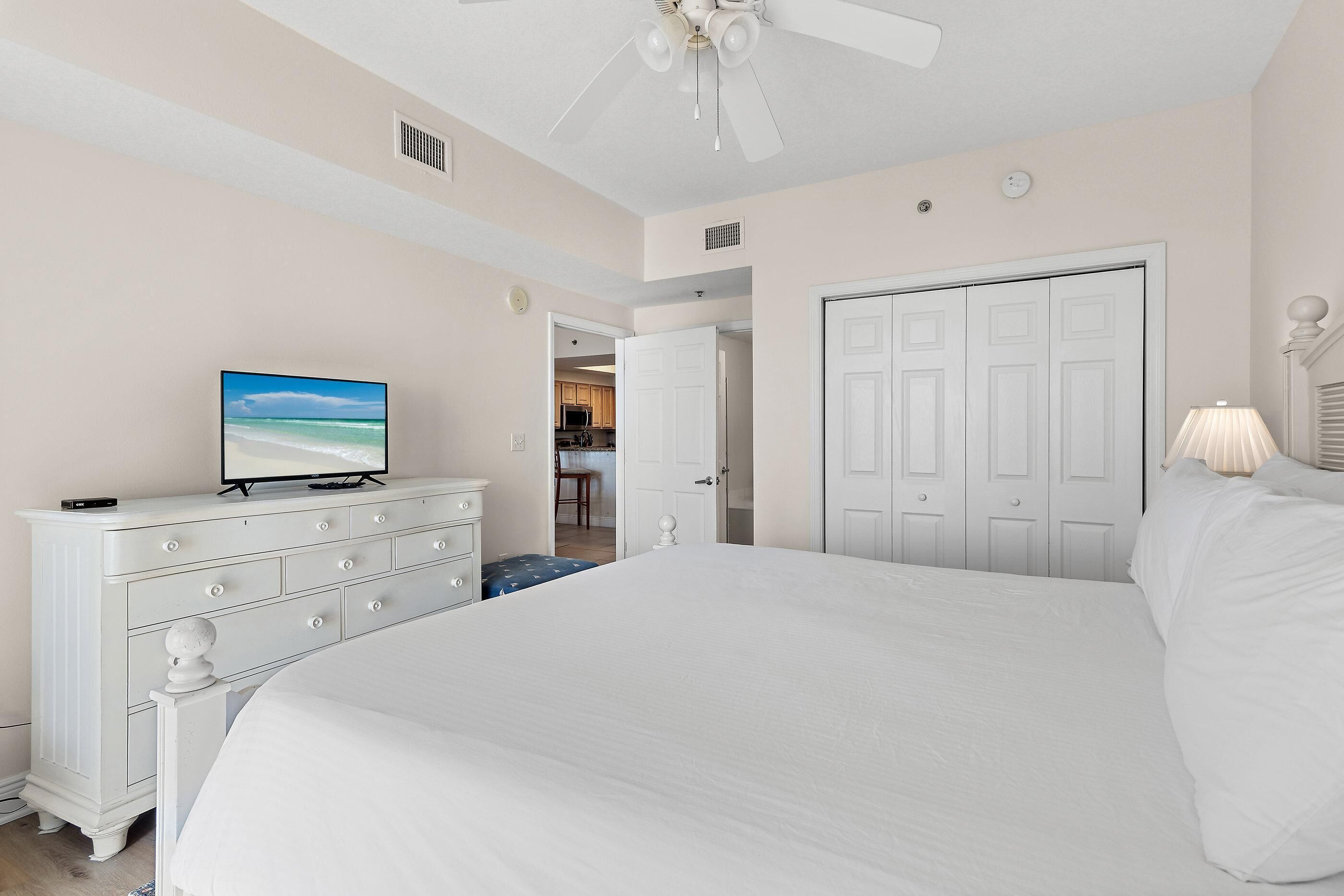 A bedroom with a large bed, a dresser, a television, and a ceiling fan.