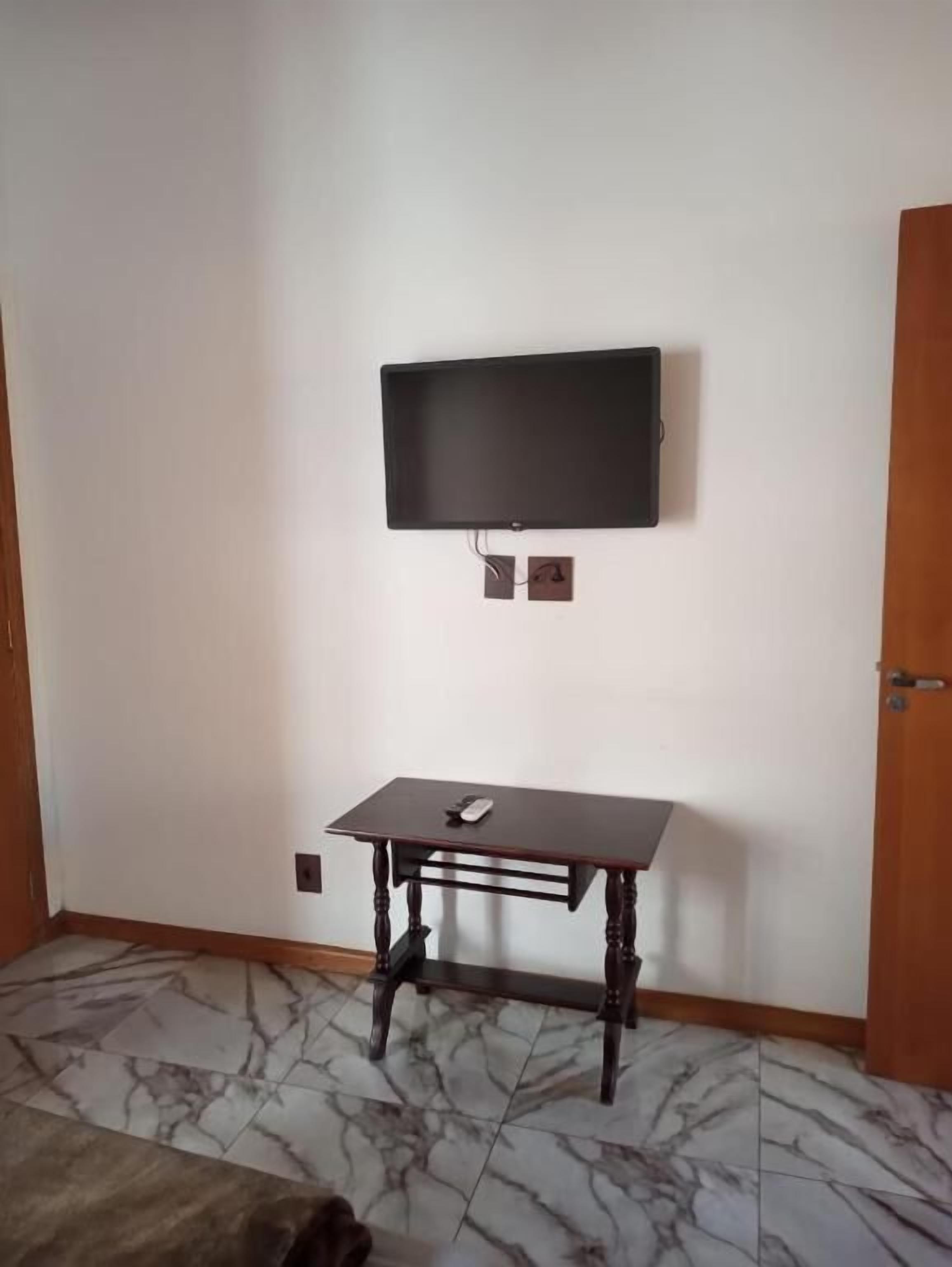 Una habitación con una televisión de pantalla plana montada en la pared, una mesa de madera con un control remoto y un piso con diseño de mármol.