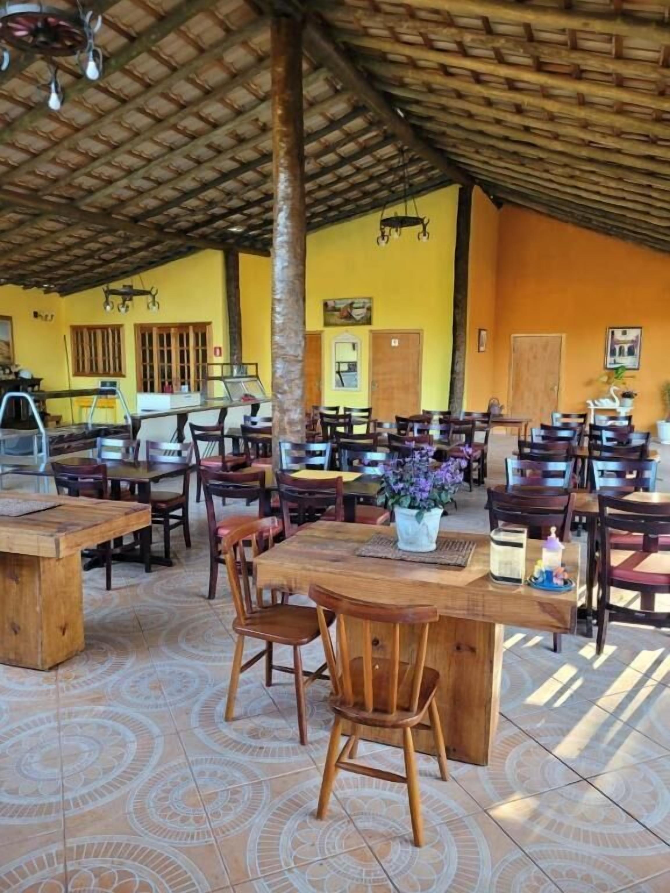 A spacious indoor dining area with multiple wooden tables and chairs, a tiled floor, and a high ceiling with a thatched roof.